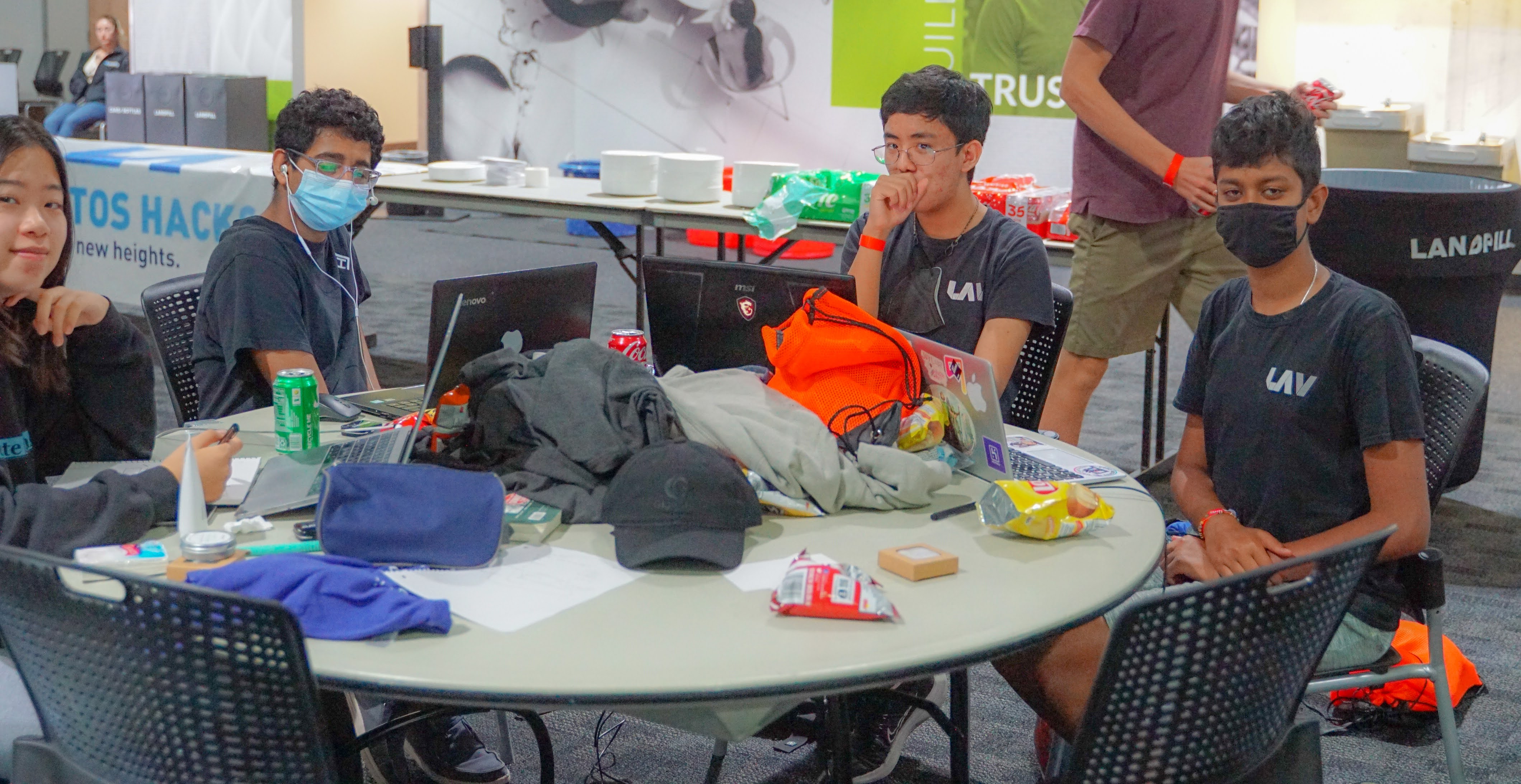 One girl and three boys, Los Altos Hacks t-shirts on and refreshments in hand, working on laptops at Los Altos Hacks VI.