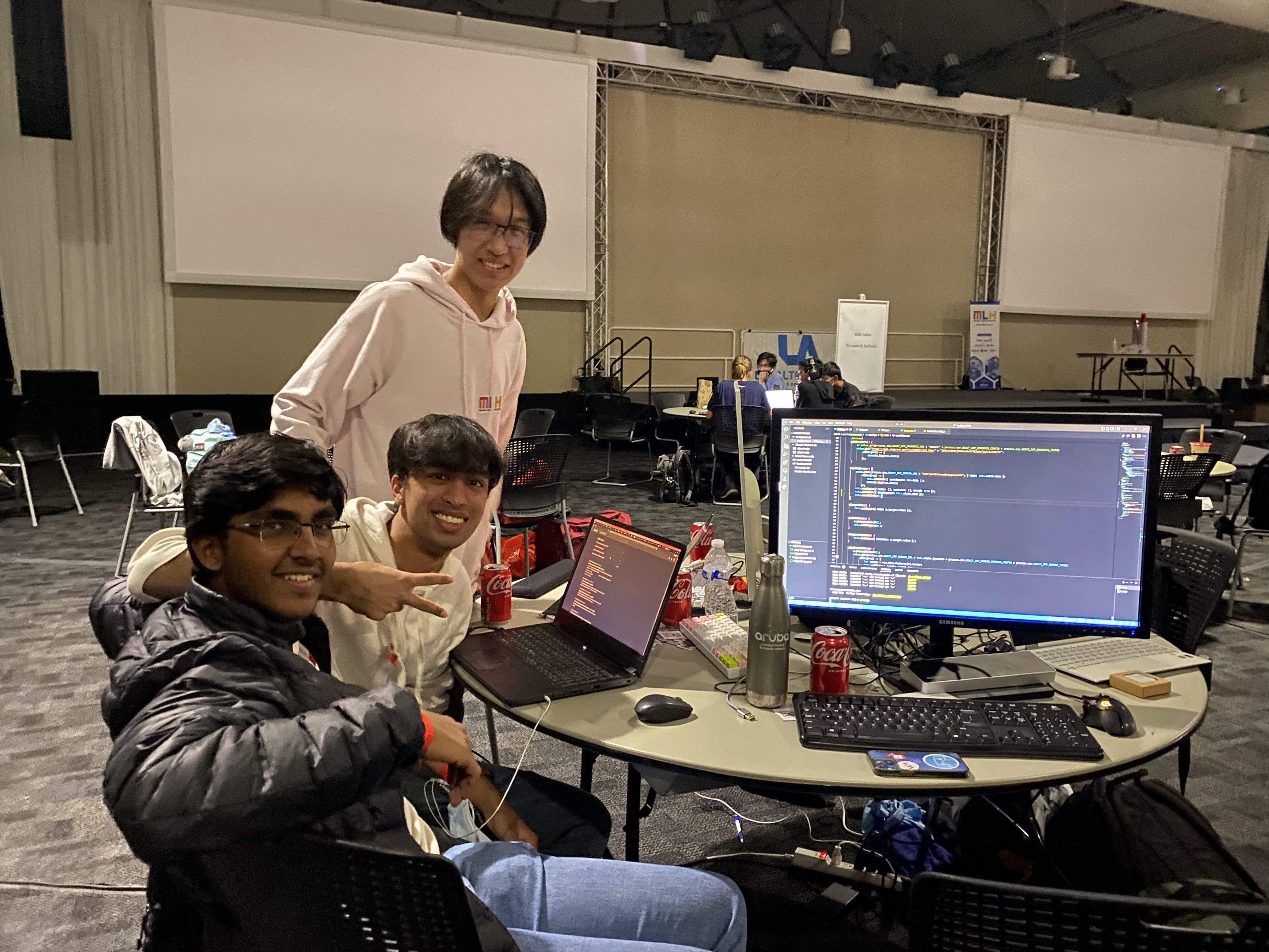 Three boys smiling and posing for a photo in front of their table at midnight at Los Altos Hacks VI.